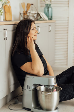 A woman cook sits on the floor and holds a professional mixer next to herの写真素材