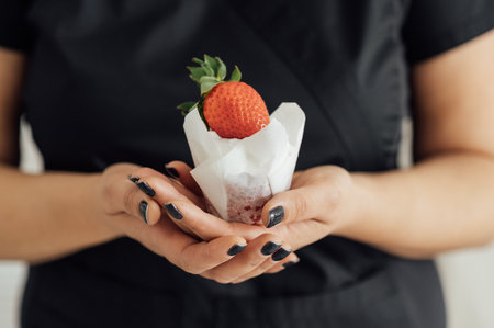 A woman in black clothes holds a cake with strawberries on top in her handの写真素材