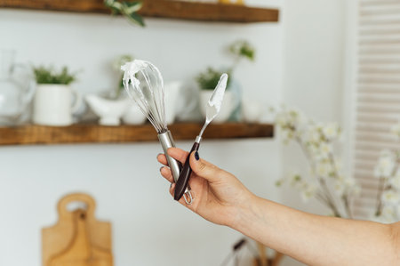 A woman cook holds a whisk and a spatula in her hand on the background of the kitchenの写真素材