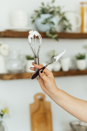A woman cook holds a whisk and a spatula in her hand on the background of the kitchenの写真素材
