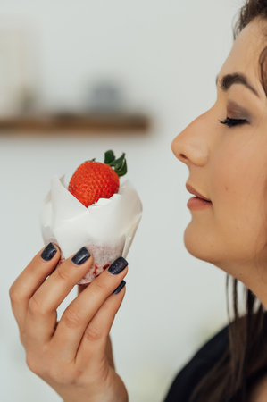 Close up portrait of pretty young brunette woman with bright make up eating tasty cake with berries and creamの写真素材