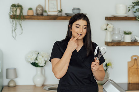 Woman cook tastes the cream for cakes whipped in a mixerの写真素材