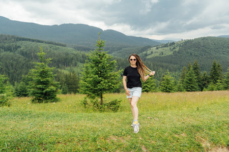 A beautiful woman with a hairstyle - a lot of braids, posing at the top of the mountain in a black T -shirt and shorts.の写真素材