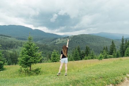 A beautiful woman with a hairstyle - a lot of braids, posing at the top of the mountain in a black T -shirt and shorts.の写真素材