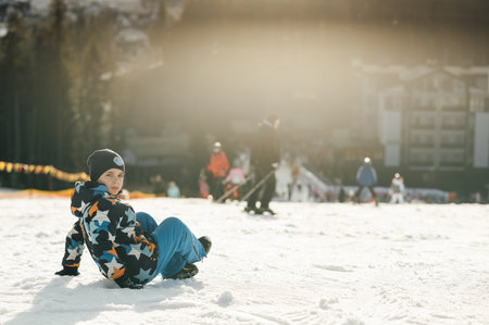 Boy Snowboarder sits on the slope of a ski descent next to a snowboardの写真素材