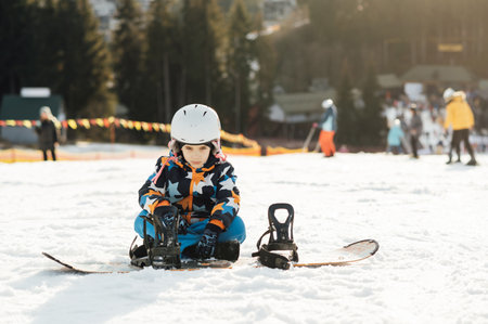 Boy Snowboarder sits on the slope of a ski descent next to a snowboardの写真素材