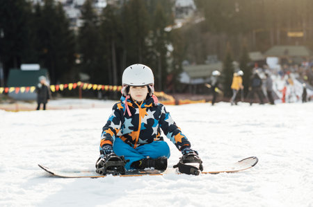 Boy Snowboarder sits on the slope of a ski descent next to a snowboardの写真素材