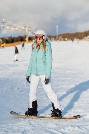A beautiful girl snowboarder stands on a slope and prepares to descendの写真素材