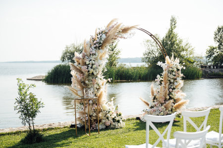 Round arch for a wedding ceremony by the river. White glass chairs stand for guestsの写真素材