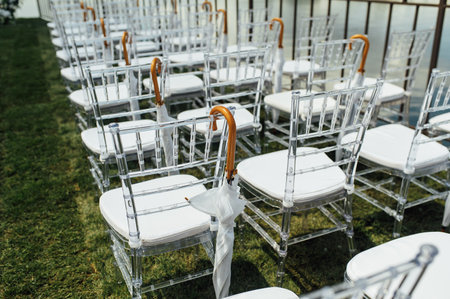 White glass chairs stand on the green grass. Round arch for a wedding ceremony in the backgroundの写真素材