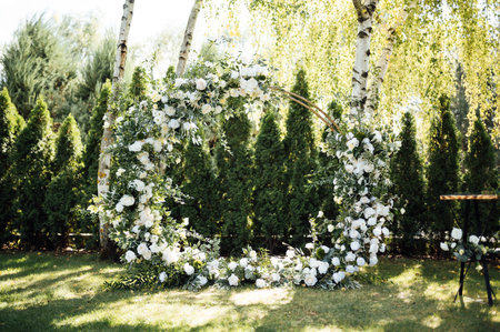 Circle wedding arch decorated with white flowers and greenery outdoors.の写真素材