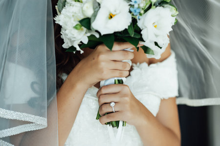 A beautiful bride holds a wedding bouquet and covers him with her faceの写真素材