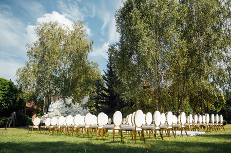 Luxury white-golden chairs on wedding ceremony outdoors. Festive decorations. Empty rows armchairs for guests.の写真素材