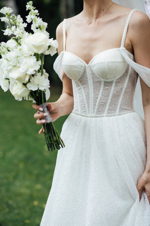 a girl in a white dress holds a wedding bouquet in her hands close-up