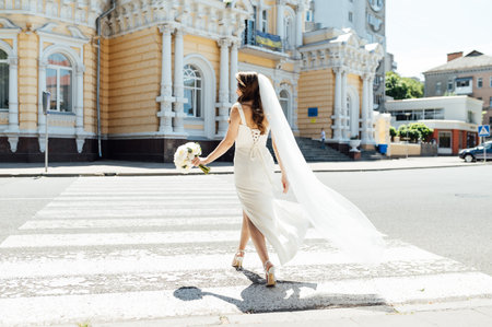 Wedding day. The bride walks along a city street in the sun. Her hair flutters beautifully in the windの写真素材