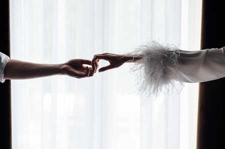 Female and male hands hold each other on a white background opposite the windowの写真素材