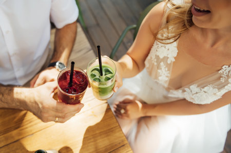 Couple drinking cocktail with slice of orange. Bride and groom holding cocktails. Honeymoon concept after wedding.の写真素材