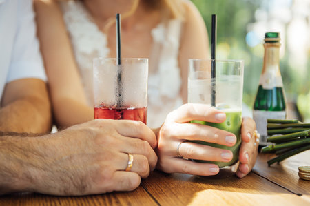 Couple drinking cocktail with slice of orange. Bride and groom holding cocktails. Honeymoon concept after wedding.の写真素材