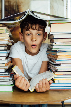A cheerful boy looks through two stacks of books. On the head is a book in the shape of a roofの写真素材