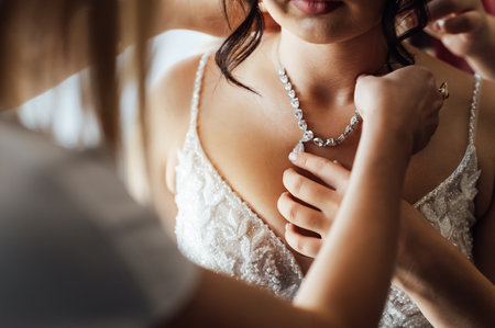 Wedding. Jewelry. The bride in a white dress putting on a necklace around her neckの写真素材