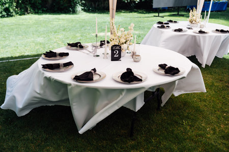 Outdoor wedding banquet. The tables are covered with tablecloths. There are various accessories and plates with napkins on the tables.の写真素材