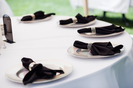 Outdoor wedding banquet. The tables are covered with tablecloths. There are various accessories and plates with napkins on the tables.の写真素材