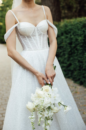 a girl in a white dress holds a wedding bouquet in her hands close-upの写真素材