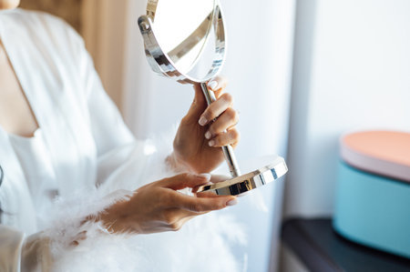 A beautiful bride holds a mirror in her hands and looks at herself. Wedding morningの写真素材