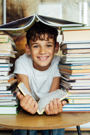 A cheerful boy looks through two stacks of books. On the head is a book in the shape of a roofの写真素材