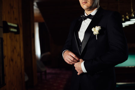 Groom in white shirt, suit and bow tie holding lapel of his jacket indoors. Wedding concept.の写真素材