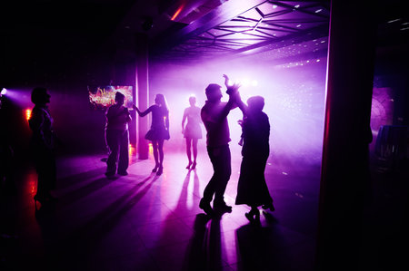 Silhouettes of people dancing and drink over colourful led screen background at nightclubの写真素材