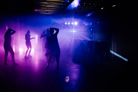 Silhouettes of people dancing and drink over colourful led screen background at nightclubの写真素材
