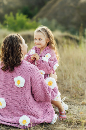 A young mother and daughter are hugging in nature among the mountains in beautiful identical sweatersの写真素材
