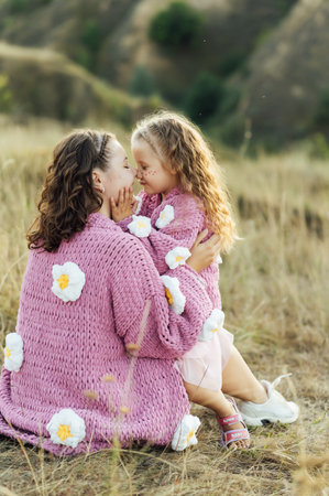 A young mother and daughter are hugging in nature among the mountains in beautiful identical sweatersの写真素材