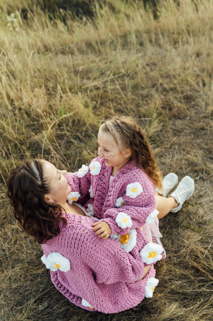 A young mother and daughter are hugging in nature among the mountains in beautiful identical sweatersの写真素材