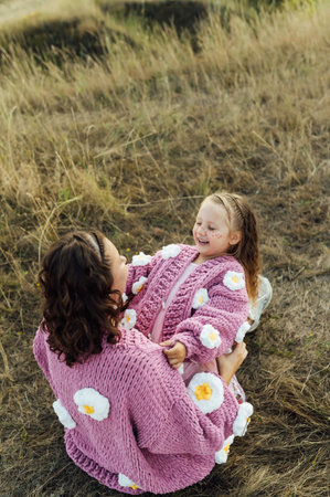 A young mother and daughter are hugging in nature among the mountains in beautiful identical sweatersの写真素材