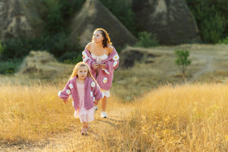 A young mother and daughter are walking in nature among the mountains in beautiful identical sweatersの写真素材