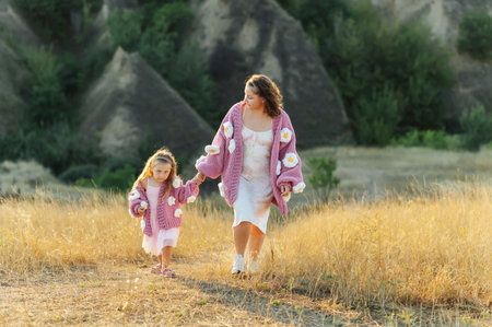 A young mother and daughter are walking in nature among the mountains in beautiful identical sweatersの写真素材
