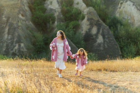 A young mother and daughter are walking in nature among the mountains in beautiful identical sweatersの写真素材