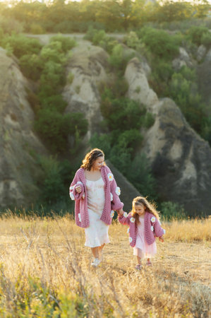A young mother and daughter are walking in nature among the mountains in beautiful identical sweatersの写真素材