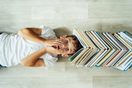 A cheerful boy lies on the floor, and above his head there is a large stack of books in the form of a roof.の写真素材