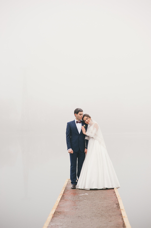 Bride hugs groom standing on  pier in cloudy weatherの写真素材