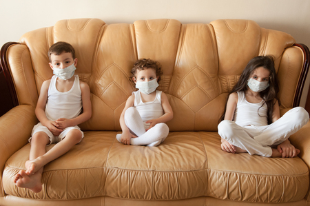 Children sit on the couch in medical masksの写真素材
