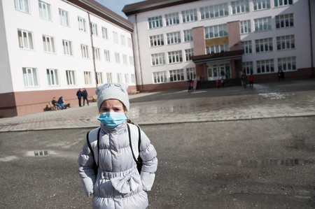 Girl is in a medical mask stands in front of schoolの写真素材