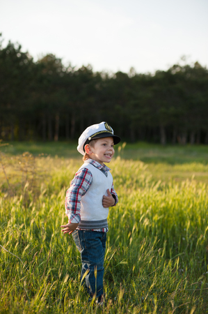 Boy in captain's hat laughs while standing in front of the forestの写真素材