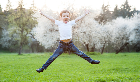 boy in jeans and t-shirt jumping and showing tongue in the parkの写真素材
