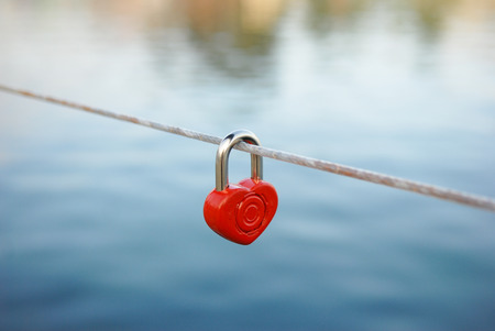 lock  in the form of heart hanging on a rope over the water