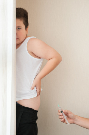 fat little boy hid behind a curtain scared by hand with syringeの写真素材