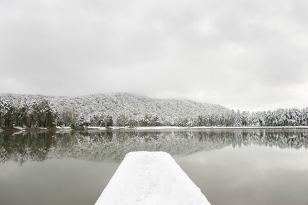 pier covered with snow against the backdrop of the lake and snowy treesの写真素材