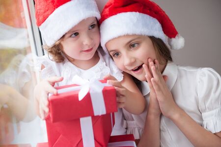 two happy little girls in Santa hats with Christmas giftsの写真素材